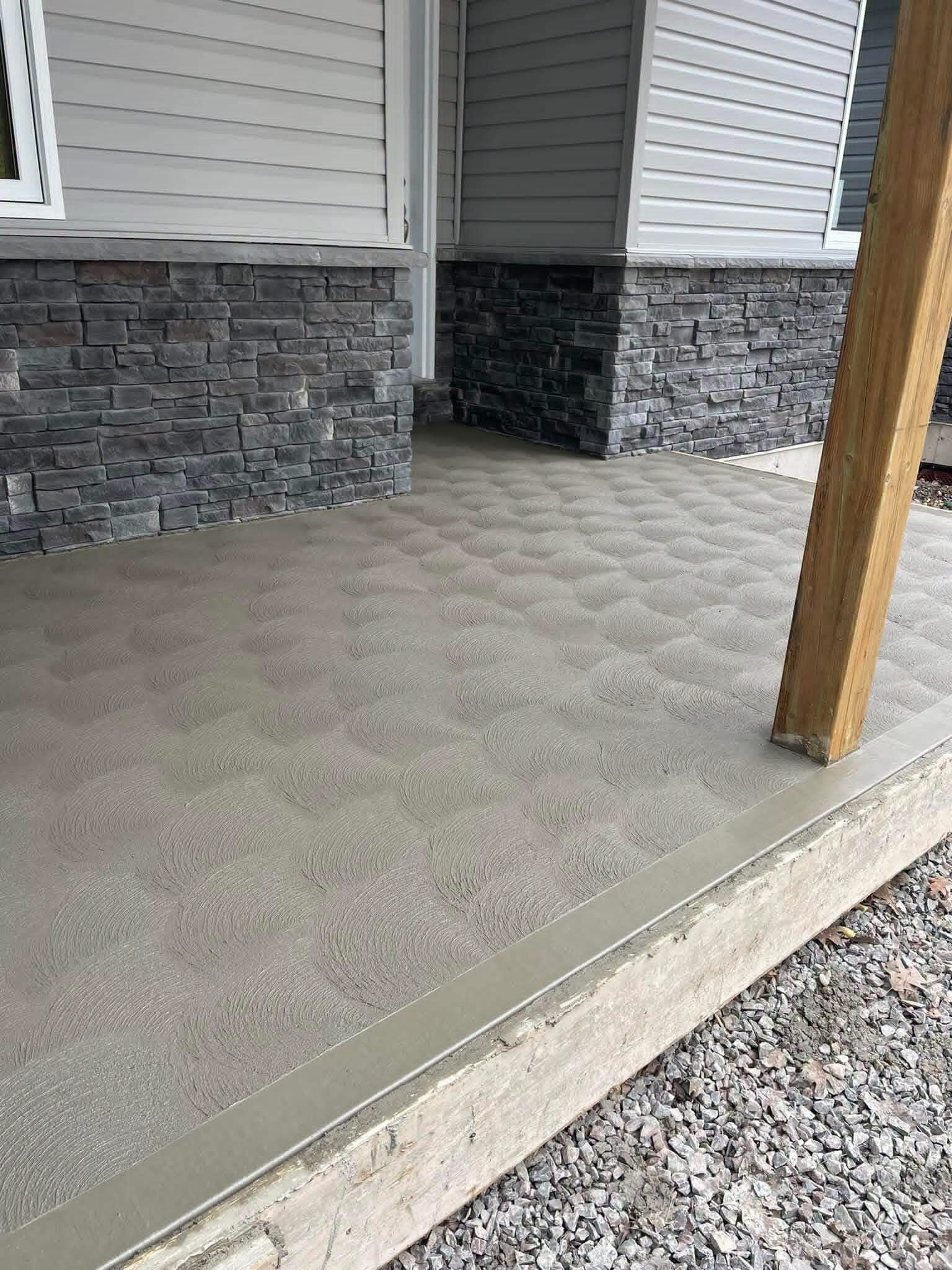 Covered brushed concrete patio beside a home