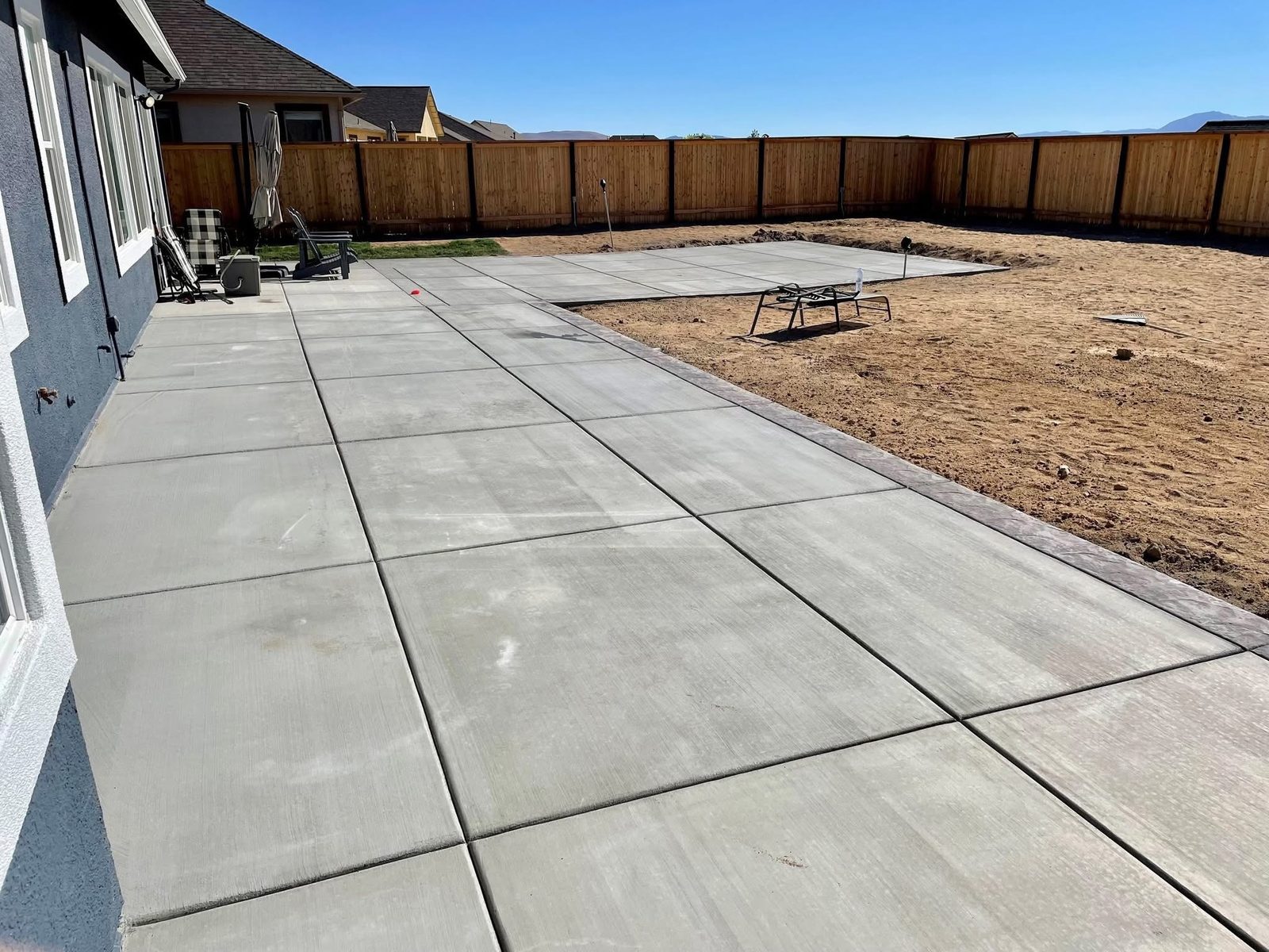 Brushed concrete patio bordered by a backyard privacy fence