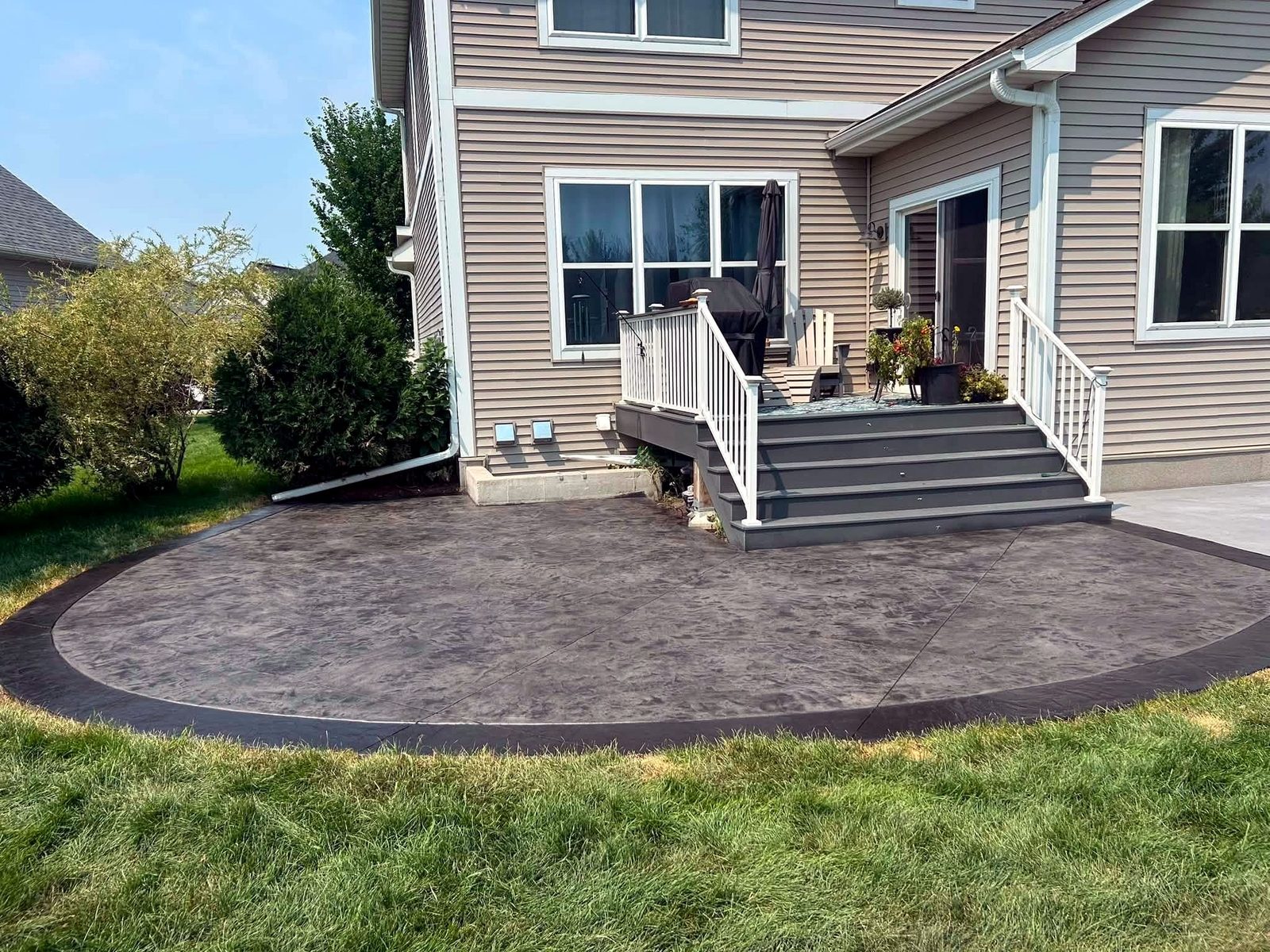 Curved concrete patio with contrasting border behind a home